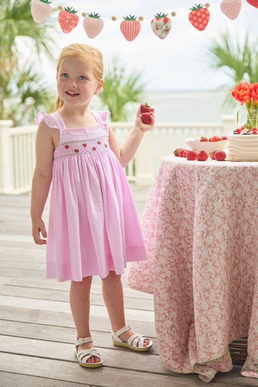 Little English traditional children's clothing. Light pink seersucker gingham dress for little girls with flutter sleeves and strawberry smocking across the chest