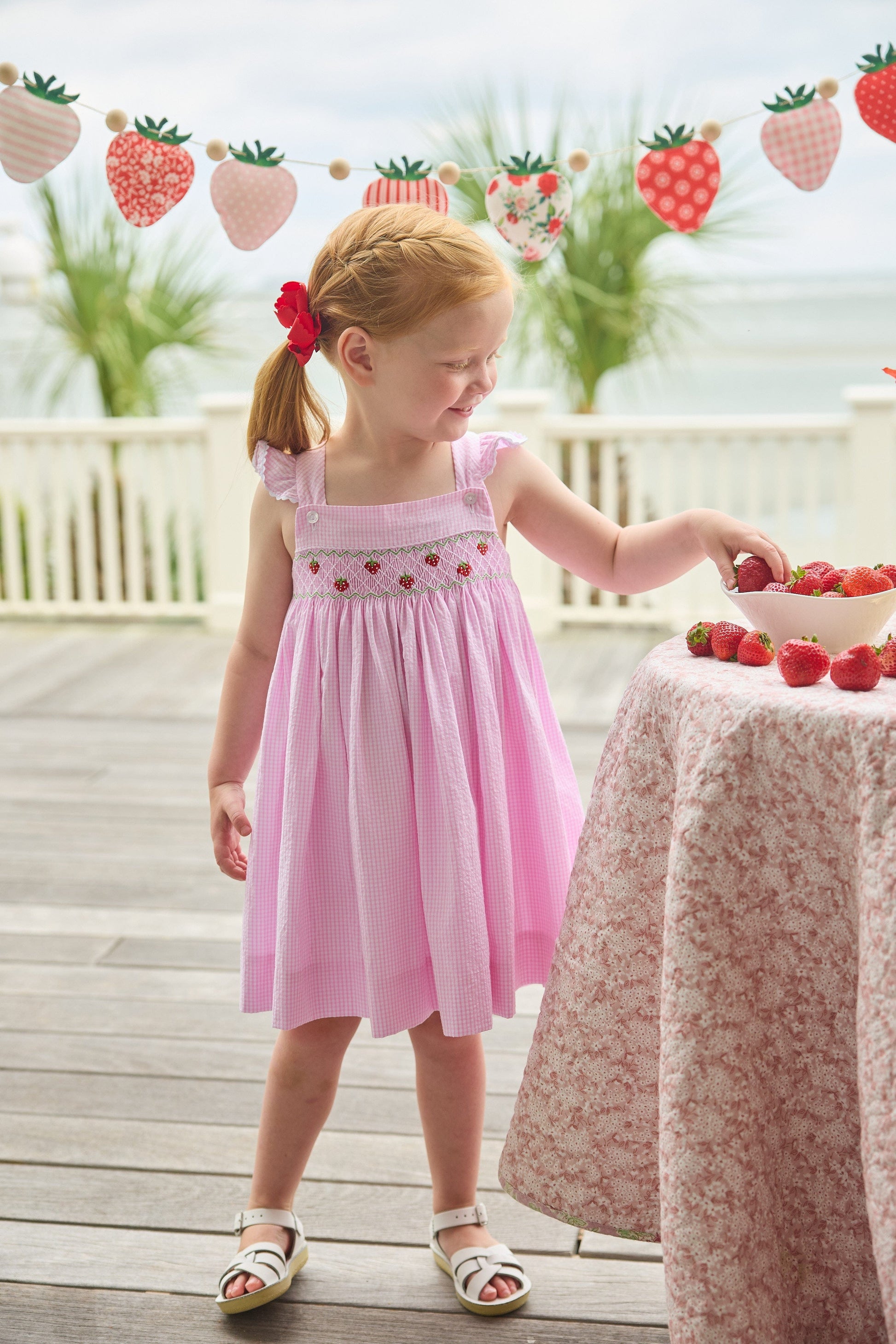Little English traditional children's clothing.  Light pink seersucker gingham dress for little girls with flutter sleeves and strawberry smocking across the chest