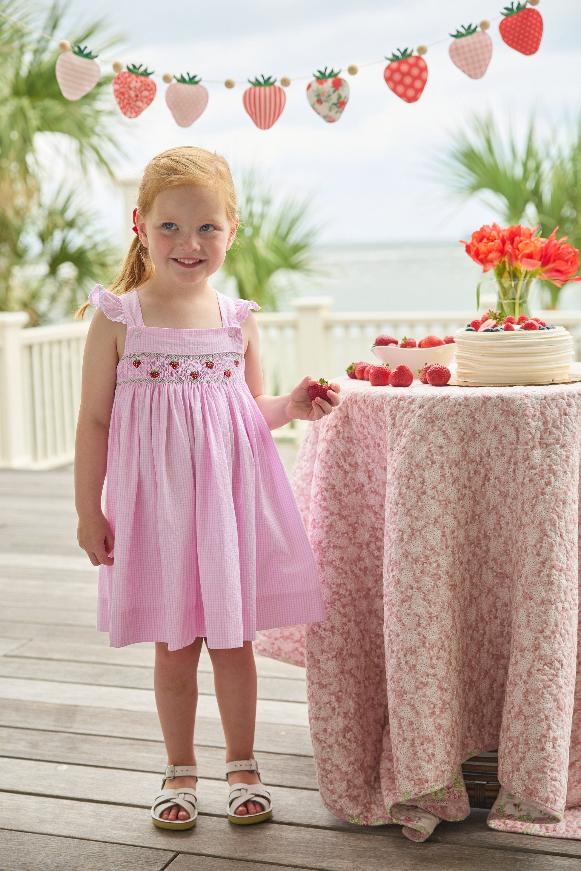 Little English traditional children's clothing.  Light pink seersucker gingham dress for little girls with flutter sleeves and strawberry smocking across the chest
