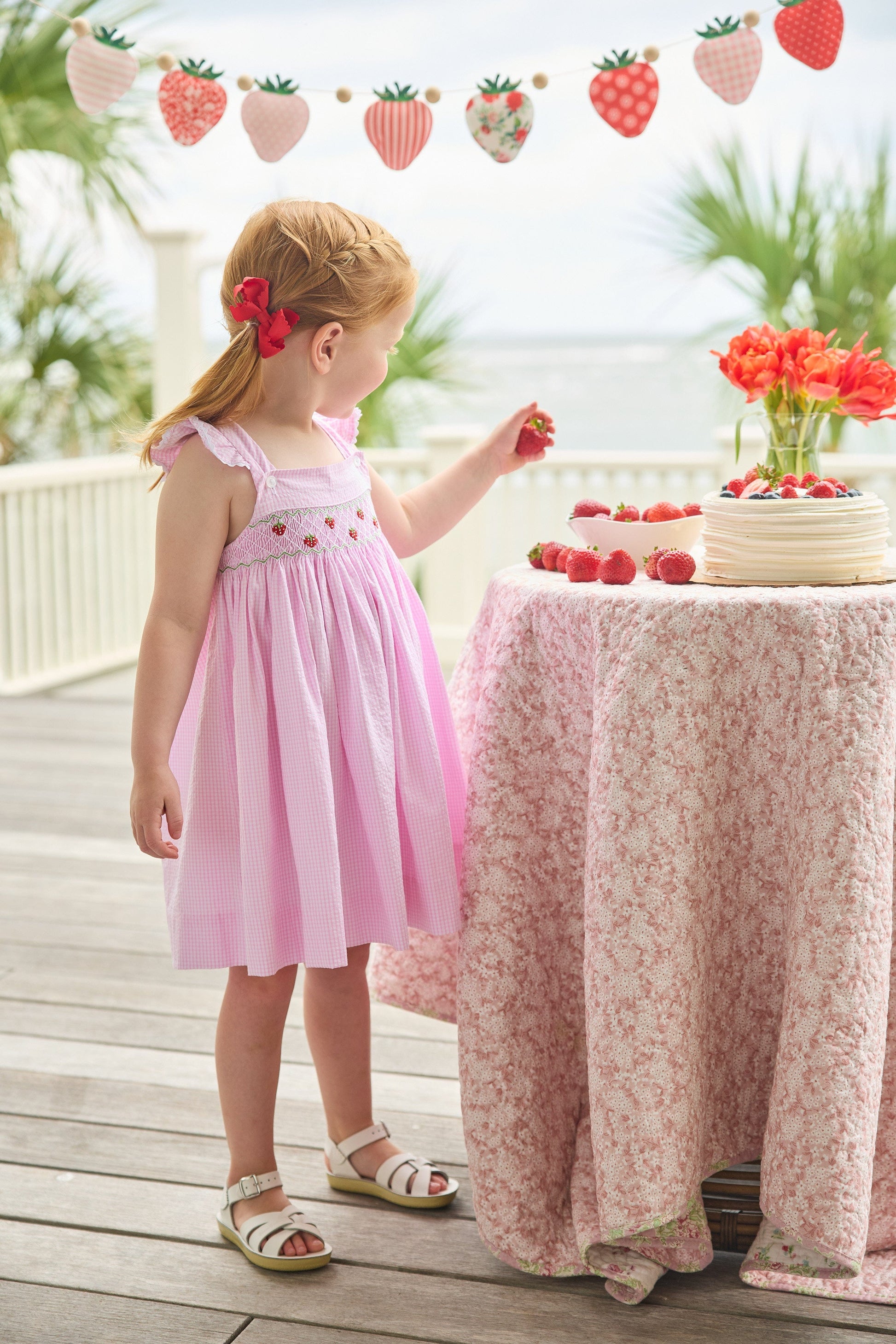 Little English traditional children's clothing.  Light pink seersucker gingham dress for little girls with flutter sleeves and strawberry smocking across the chest
