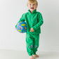 Laughing toddler holding a ball, wearing the green Tow Truck Scout Quarter Zip and Adventure Joggers
