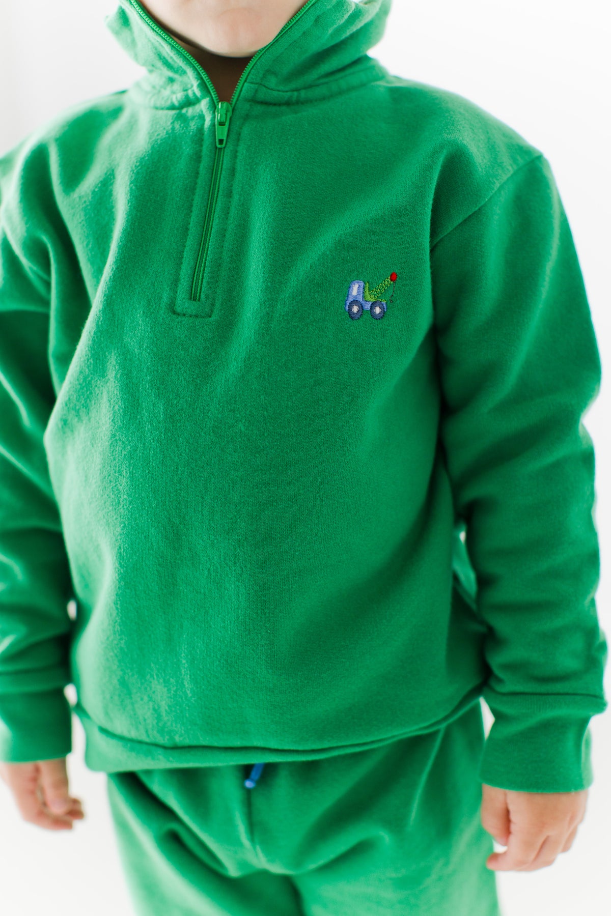 Close-up of the embroidered tow truck on the chest of the green Scout Quarter Zip