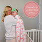White muslin swaddle blanket with pink bow print, draped over a baby held by their mother in a nursery