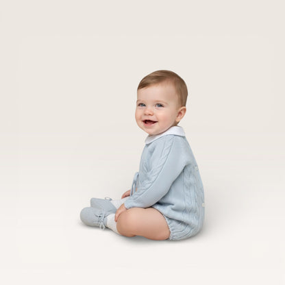Baby wearing a light blue knitted outfit on a white background