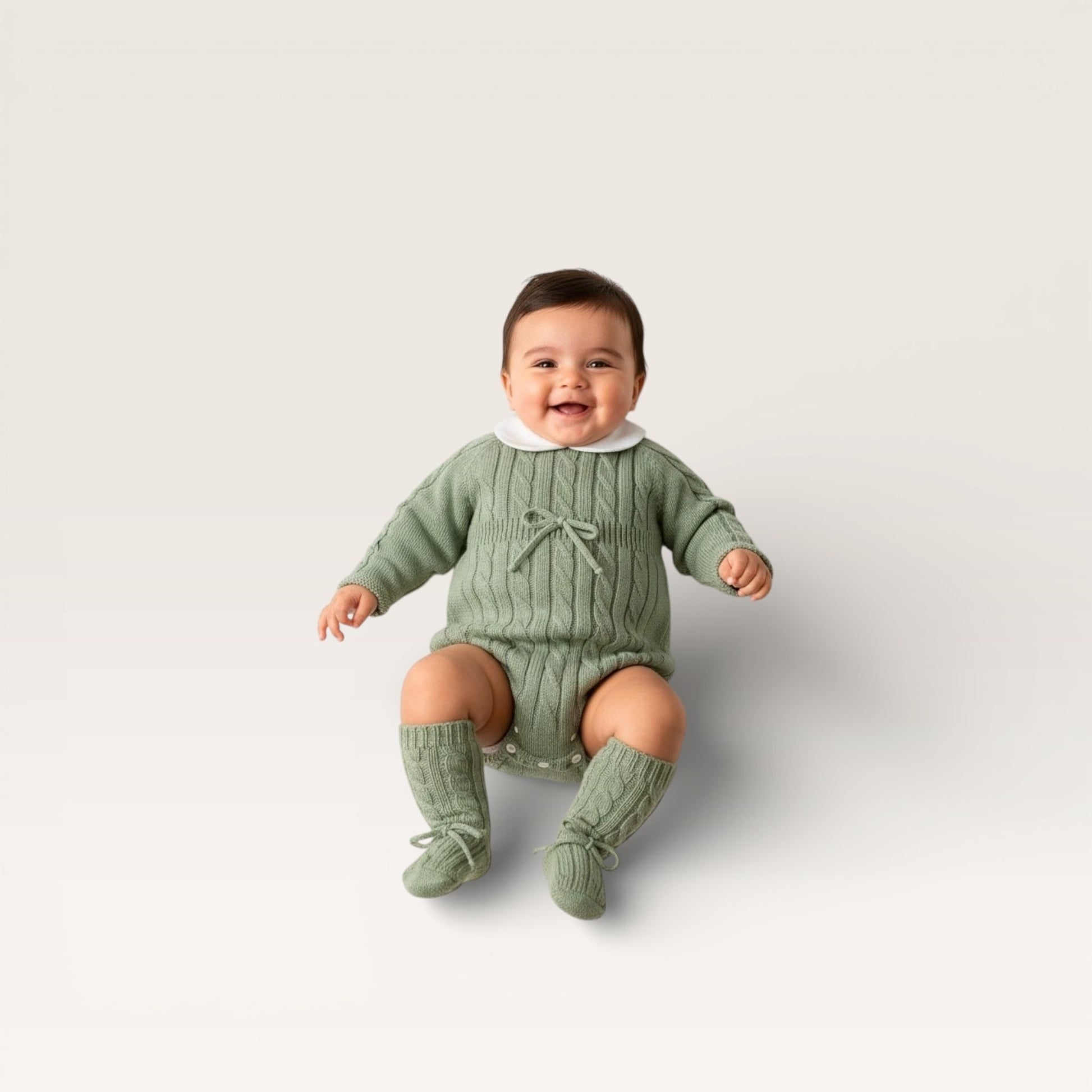 Baby wearing a green outfit with matching socks on a light gray background