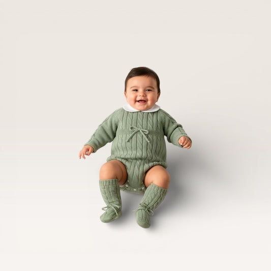 Baby wearing a green outfit with matching socks on a light gray background