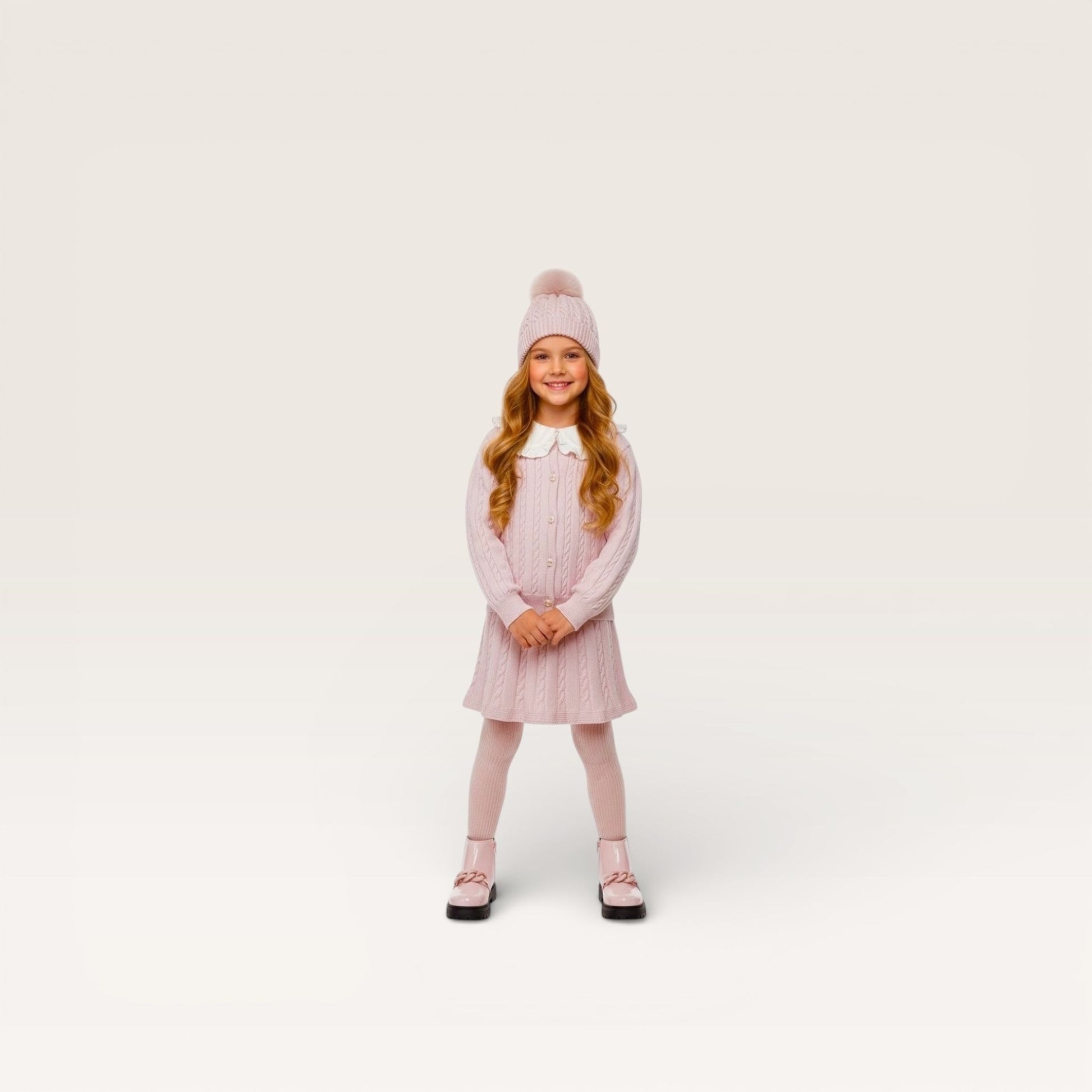 Young girl wearing a pink knitted dress and hat on a white background