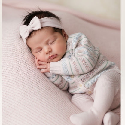 Newborn baby sleeping on a pink blanket wearing a knitted outfit and headband.