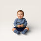 Baby wearing a blue sweater and matching booties sitting on a light gray background