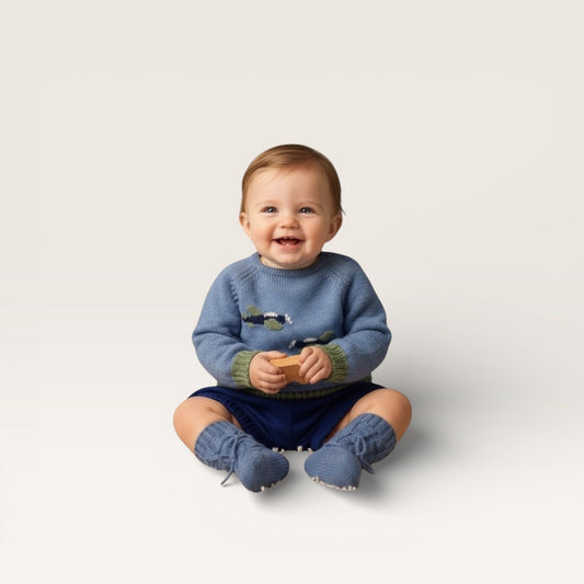 Baby wearing a blue sweater and matching booties sitting on a light gray background