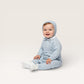 Baby wearing a light blue knitted outfit with a matching bonnet on a white background