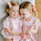 Two young girls in matching pink princess dresses sitting on a couch.