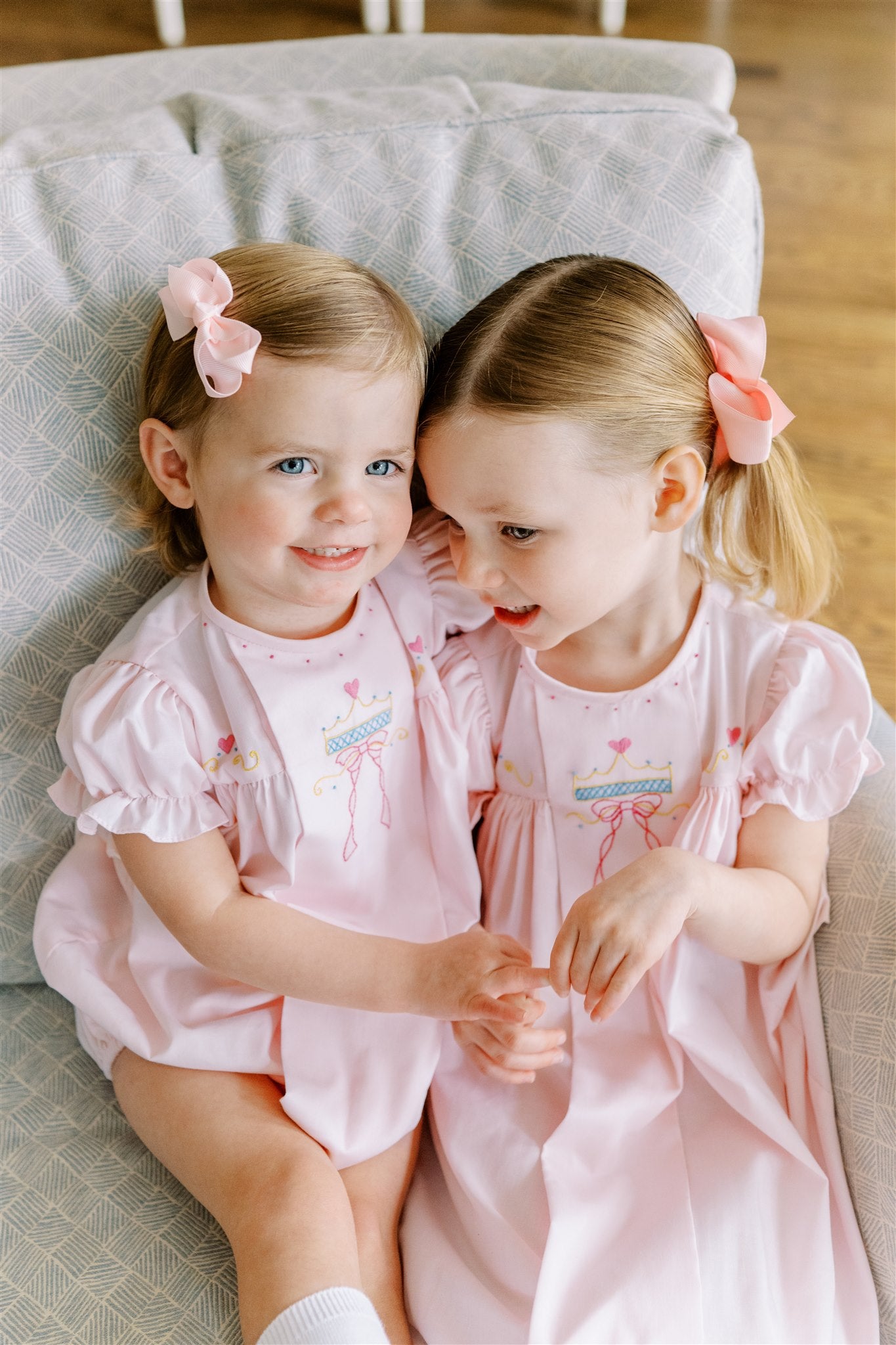 Two young girls in matching pink princess dresses sitting on a couch.