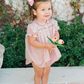 Young girl in a pink onesie with floral embroidery holding flowers outdoors