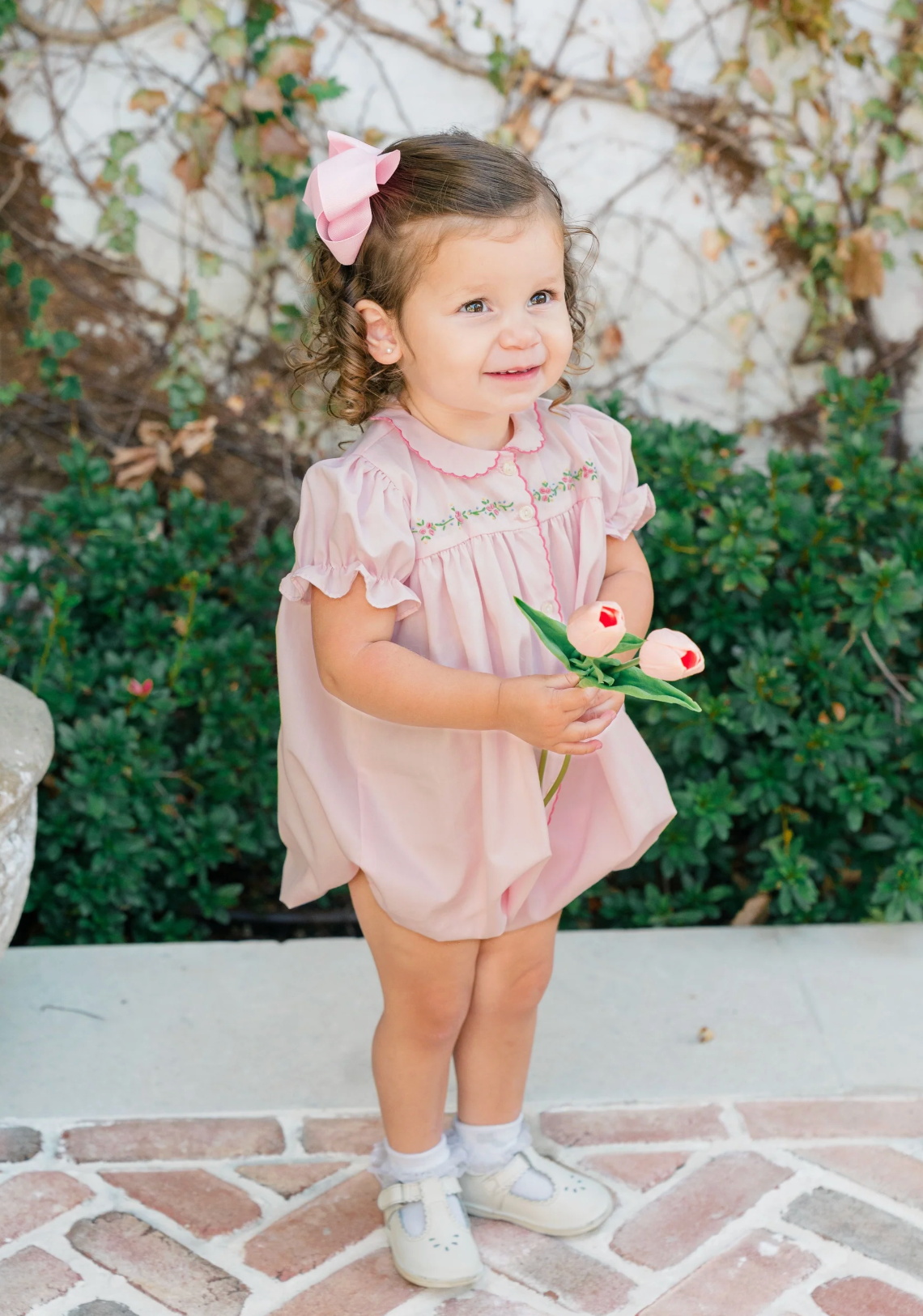 Young girl in a pink onesie with floral embroidery holding flowers outdoors