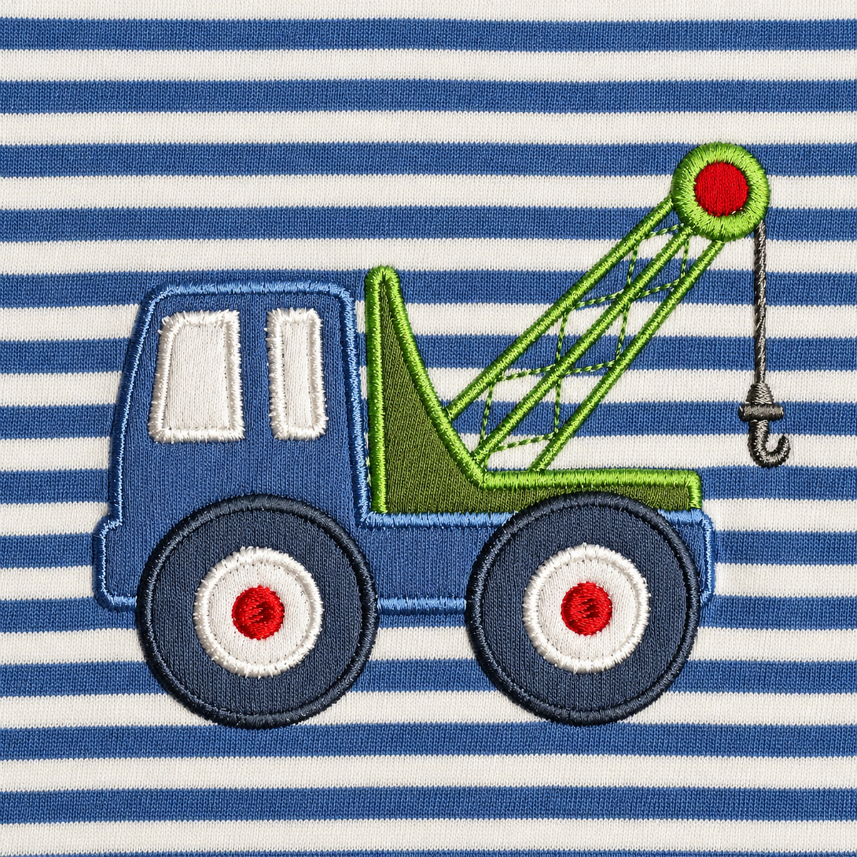 Close-up of the stitched tow truck appliqué with green crane arm, hook and red wheel hubs on blue and white stripes