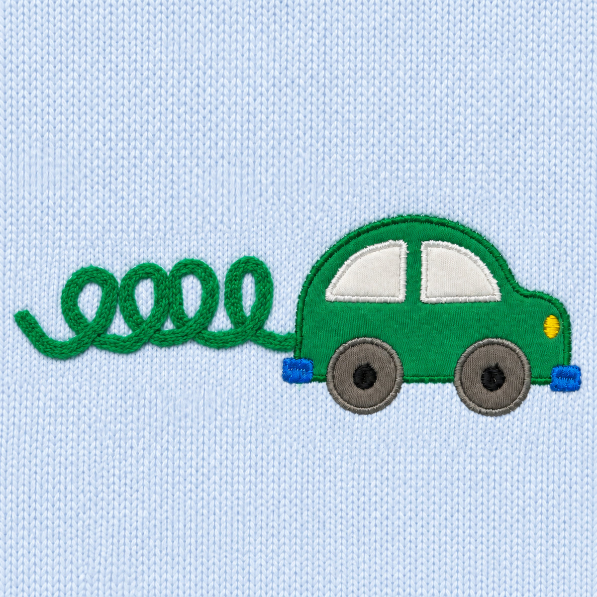 Close-up of the green car appliqué with stitched windows, grey wheels and looping green exhaust trail on light blue knit